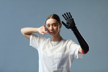 Portrait of girl with disability with prosthetic arm standing against on blue background - obrazy, fototapety, plakaty
