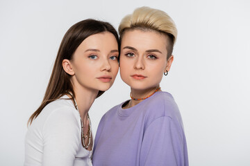 young and pretty lesbian couple with beads and makeup looking at camera isolated on grey.