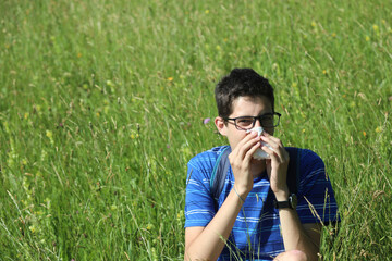 young boy with glasses blowing his nose because of allergy in the meadow