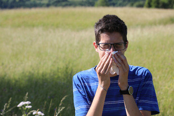 young boy with glasses blowing his nose because of allergy in the meadow