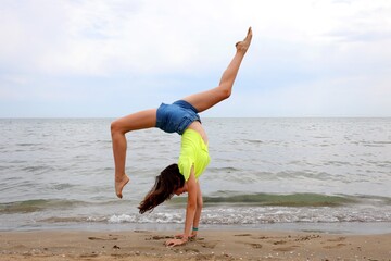 girl on the foreshore of the sea while performing gymnastic exercises with her head upside down