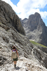Fototapeta premium woman hiker with backpack on shoulders walks on stone path in high Dolomites mountain of european alps