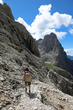 woman hiker with backpack on shoulders walks on stone path in high Dolomites mountain of european alps