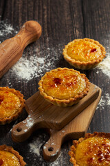 A close-up of delicious tarts with caramelized tops, resting on a wooden cutting board amid a dusting of flour