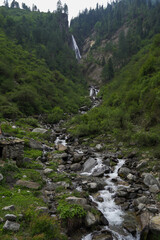 Fototapeta na wymiar Beautiful and spectacular natural waterfall falling through rocky mountains enroute har ki dun valley. A perfect morning landscape of lush green and rocky mountains and powerful waterfall.