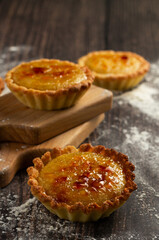 Golden-baked custard tarts with a sprinkle of powdered sugar on top, resting on a wooden board with a rustic charm
