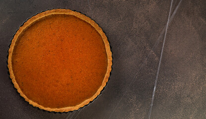 A full, smooth pumpkin pie sits on a dark background, its rich orange color a promise of classic fall flavors
