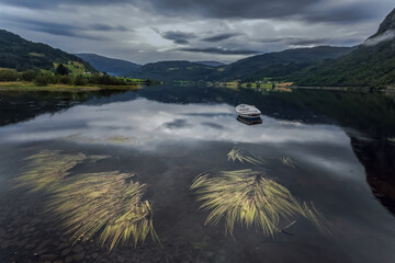 Idyllic lake landscape surrounded by mountain peaks. Lonely boat in the middle of the lake.