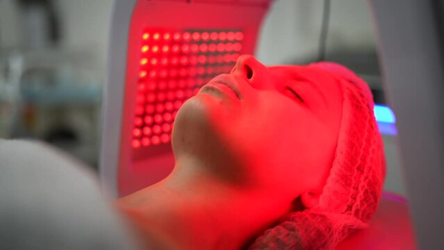 Close up of young woman having red and blue LED light facial therapy treatment in beauty salon while laying on a couch and relaxing. Beauty, healthcare and wellness concept. Cosmetology and Skin Care.