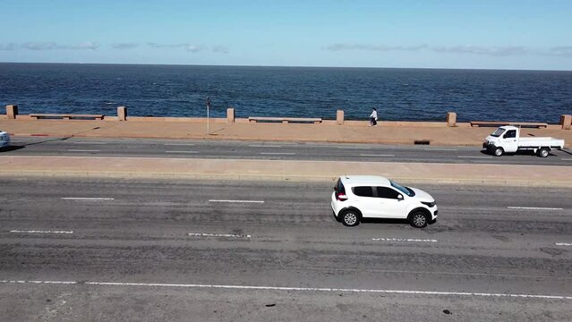 Street aerial side view with cars and girl passing in rambla promenade of Montevideo, Uruguay