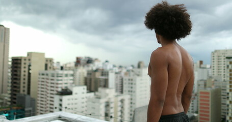 Fototapeta na wymiar Young mixed race man standing shirtless on top of rooftop looking at city