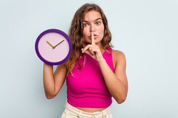 Young caucasian woman holding a clock isolated on blue background keeping a secret or asking for...