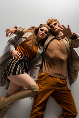 top view of stylish young couple in autumnal outfits and sunglasses lying together isolated on grey.