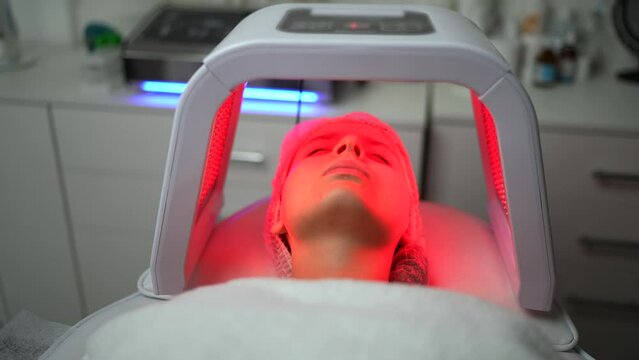 Close up of young woman having red and blue LED light facial therapy treatment in beauty salon. Woman laying on a couch and relaxing while LED light session. Beauty, healthcare and wellness concept.