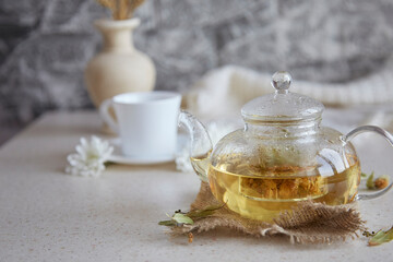 Organic linden tea in teapot with cup of tea. Relaxing teatime. Eco-friendly sustainable lifestyle. Wheat, chrysanthemums, autumn decorations and notebook. Cozy atmospheric home.