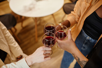 Above angle of young multicultural friends clinking with glasses of red wine while standing in front of one another at home party