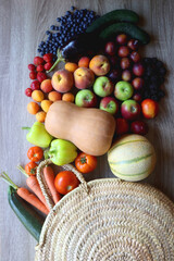 Round straw bag and various healthy fruits and vegetables on wooden background.