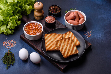Traditional English breakfast with eggs, toast, sausages, beans, spices and herbs on a grey ceramic plate