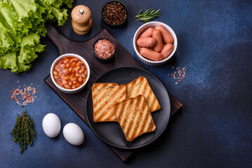 Traditional English breakfast with eggs, toast, sausages, beans, spices and herbs on a grey ceramic plate