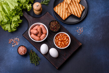 Traditional English breakfast with eggs, toast, sausages, beans, spices and herbs on a grey ceramic plate
