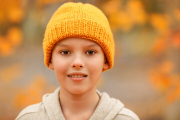 Boy in a hat is smiling in the autumn park. Bright colour background. Close up portrait of a cheerful boy.