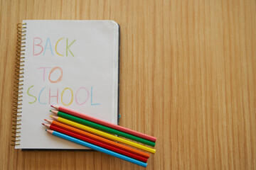 Back to school notebook with color pencils over wooden table