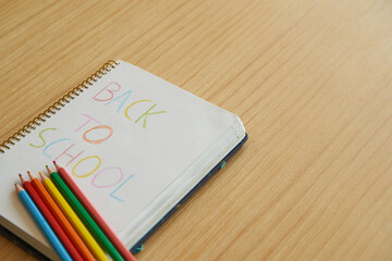 Kids notebook with back to school message with color pencils over wooden table with copyspace