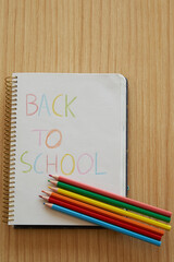 vertical shot of Kids notebook with back to school message with color pencils over wooden table