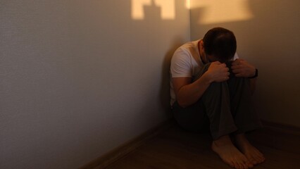 alone depressed man sitting in corner dark room because of problem and sadness in life. Sadnes and...
