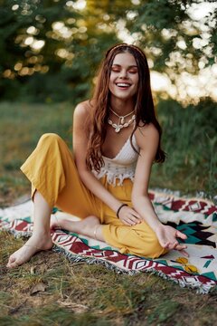 A young beautiful hippie woman sits on the ground in the fall in eco clothing in the sunset light and smiles sincerely for the camera