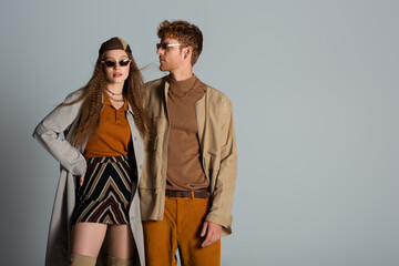 stylish couple in autumnal outfits and trendy sunglasses standing isolated on grey.