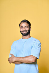 Smiling confident bearded indian man standing isolated on yellow background. Happy handsome ethnic guy wearing blue t-shirt looking at camera posing with arms crossed, vertical portrait.