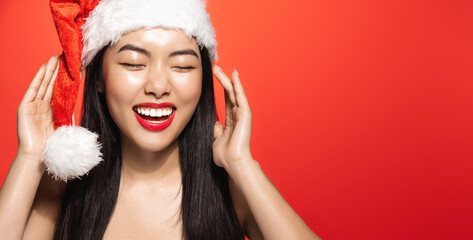 Portrait of beauty asian girl laughing and smiling, celebrating winter holidays in christmas hat, red background