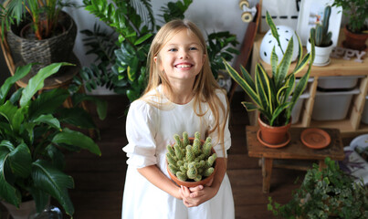 Happy blonde girl in a white dress among the house plants