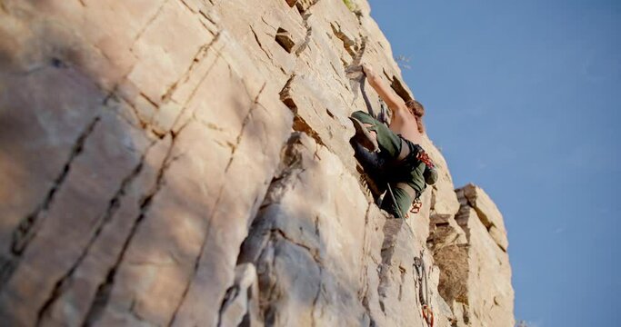 
Male rock climber on wall takes a step on rock to climb higher