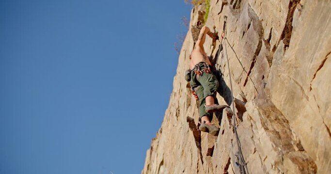 Male rock climber chalks up on wall, takes step