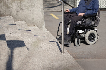 Person with disability on electric wheelchair stopping at the bottom of inaccessible staircase,...