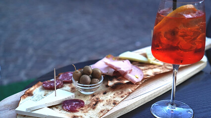 Close up of italian appetizers and spritz table with woman's hand taking olive from the plate,...