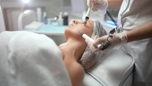 Beautician conducting facial microcurrent therapy for rejuvenating and tightening skin of beautiful caucasian woman client at beauty salon. Non surgery cosmetology, professional skincare concept.