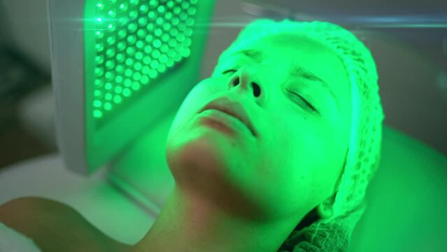 Portrait of young woman having green LED light facial therapy treatment in beauty salon. Beauty, healthcare and wellness concept. Cosmetology and Skin Care. High quality 4k footage