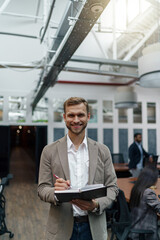 Businessman standing in office and making notes against background of colleagues 