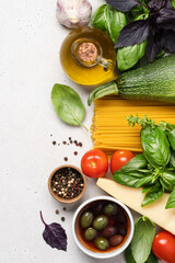 Italian food on white background. Fresh green and red basil, tomatoes, parmesan cheese, olives, olive oil, spices, spaghetti pasta, zucchini. Ingredients for cooking vegan dishes