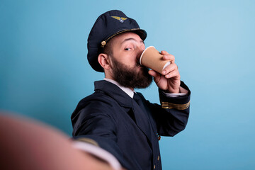 Aviator drinking coffee to go first person view, taking photo on front camera, fpv. Middle aged airlane pilot in uniform holding take away tea paper cup pox, making selfie on smartphone