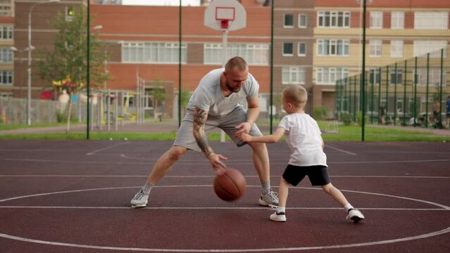 Father and son are playing together basketball outdoors on court in the city.