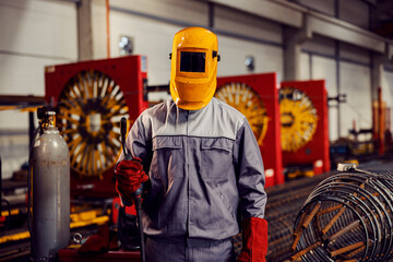 A metallurgy worker, with a protective mask, stands in the facility and shows a welding machine.