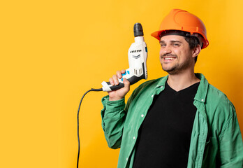Guy in helmet with drill on yellow background