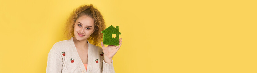Happy house buyer. A young girl holds a model of a green house in her hands. The concept of green...
