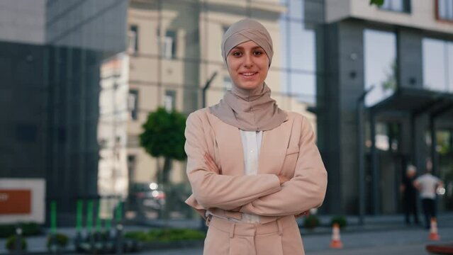 Portrait of the arabian woman wearing hijab standing with crossing arms smiling looking at the camera on the business centre background. Concept of business and career