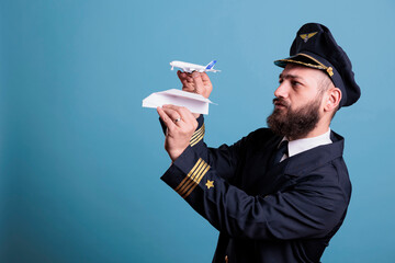 Airplane aviator holding jet toy and paper plane in hands front view, pilot demonstrating aircraft crash with aeroplane model. Professional aviation academy aviator on blue background © DC Studio