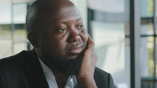 Sad unhappy dreamy afro american overweight plus size bearded man businessman feel boredom lack of motivation sit in office look at distance dream about ending of working day tired from monotone work